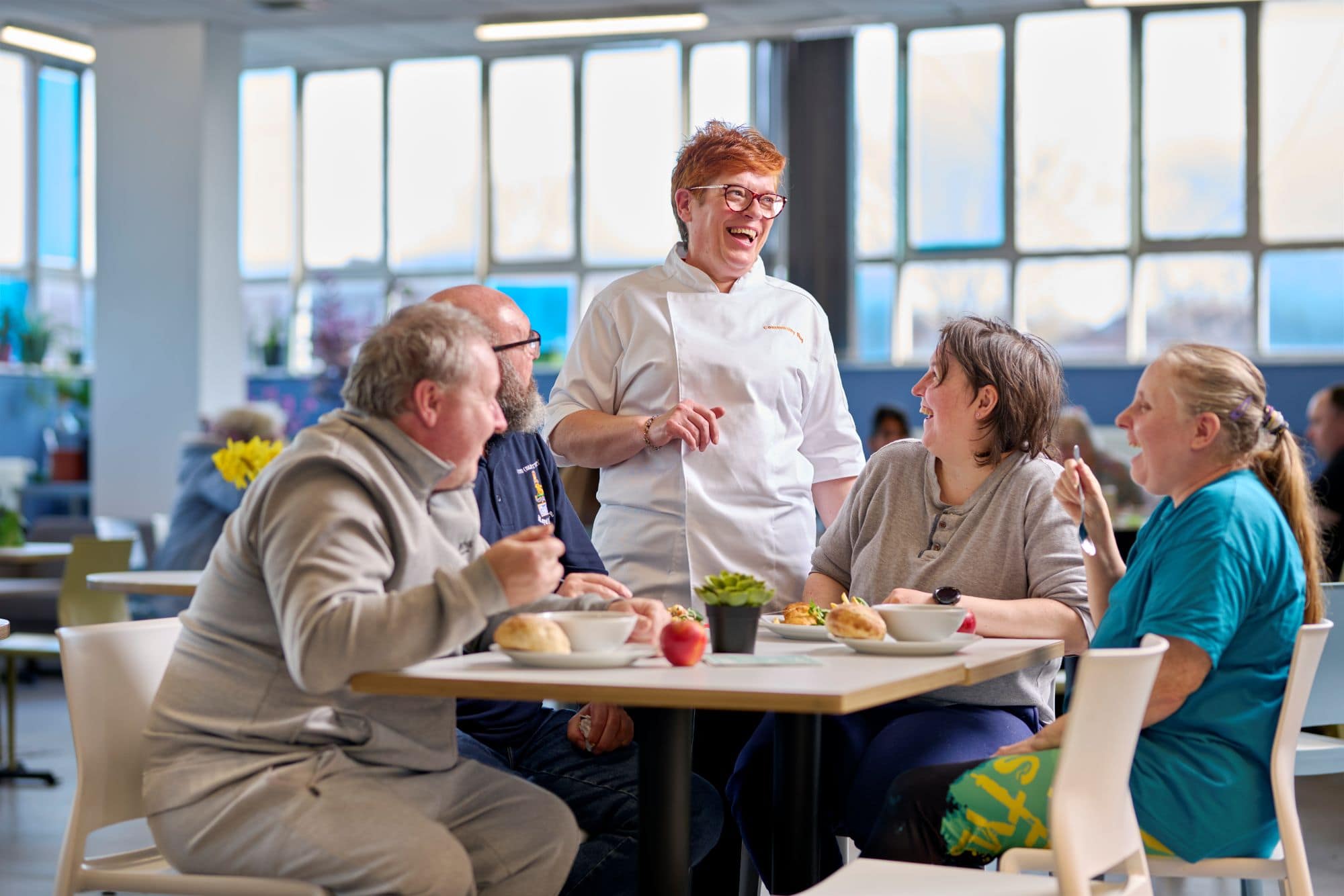 Customers sat around table with Community kitchen chef