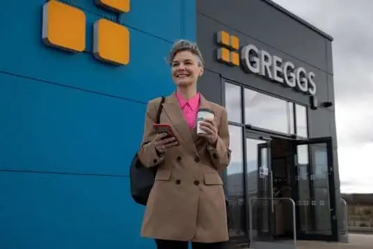 Person with coffee in front of Greggs store