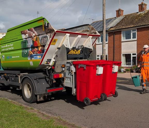 Bin lorry being operated by employee emptying red smart bins
