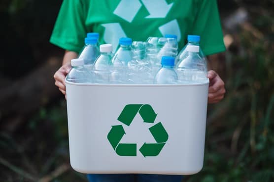 A woman collecting garbage and holding a recycle bin with plastic bottles in the outdoors